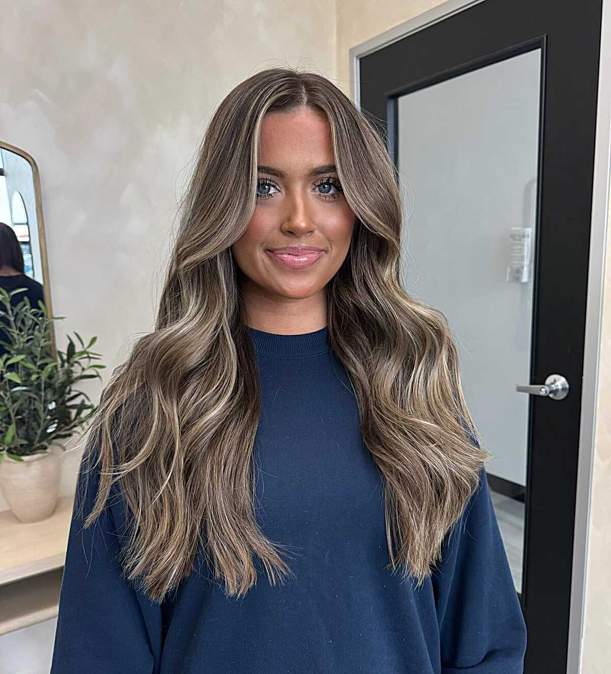 Long cool-toned bronde waves with a centered part and dark root.
