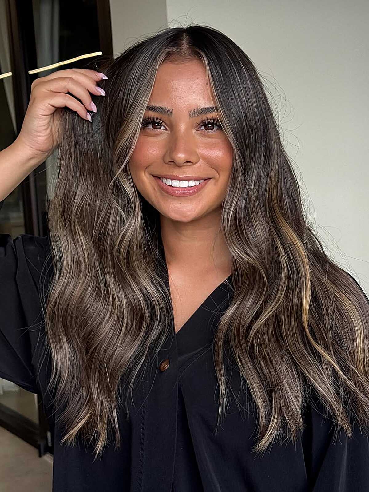 Long bronde balayage with dark roots and scattered cool highlights.