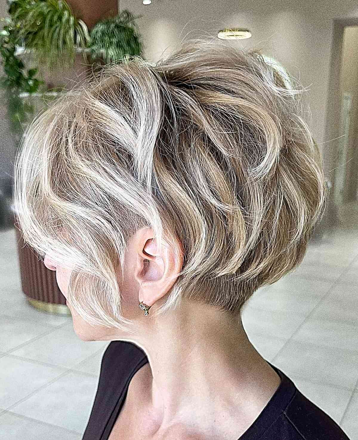 Wavy honey blonde pixie bob with a short undercut and layered top.