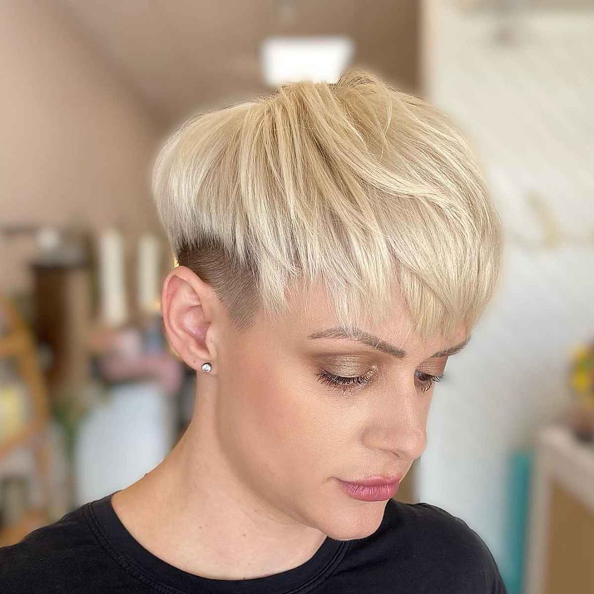 Short blonde pixie with blunt fringe and cropped sides.