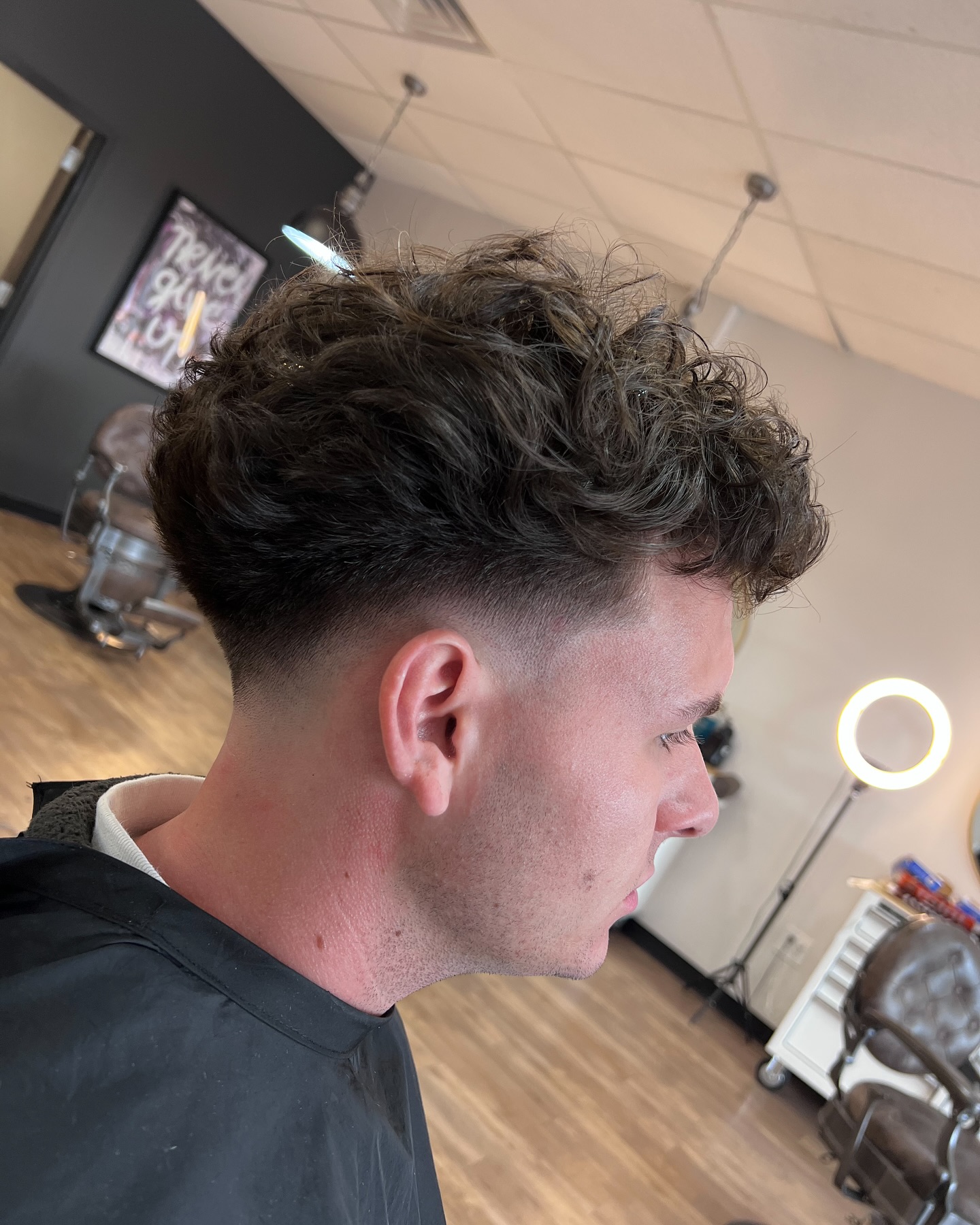 High curly top with tight fade and rounded shape.