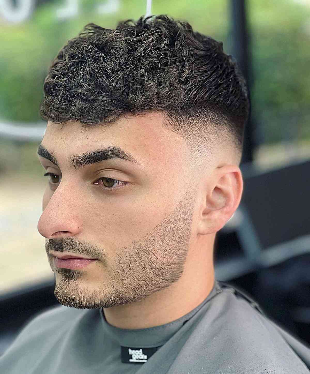 Short curly top with a blunt-looking fringe and faded sides.