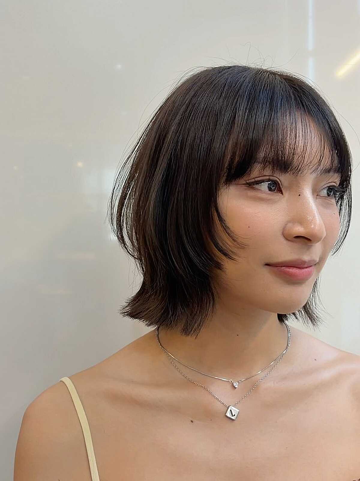 Jaw-length dark bob with thin bangs and softly flipped ends.