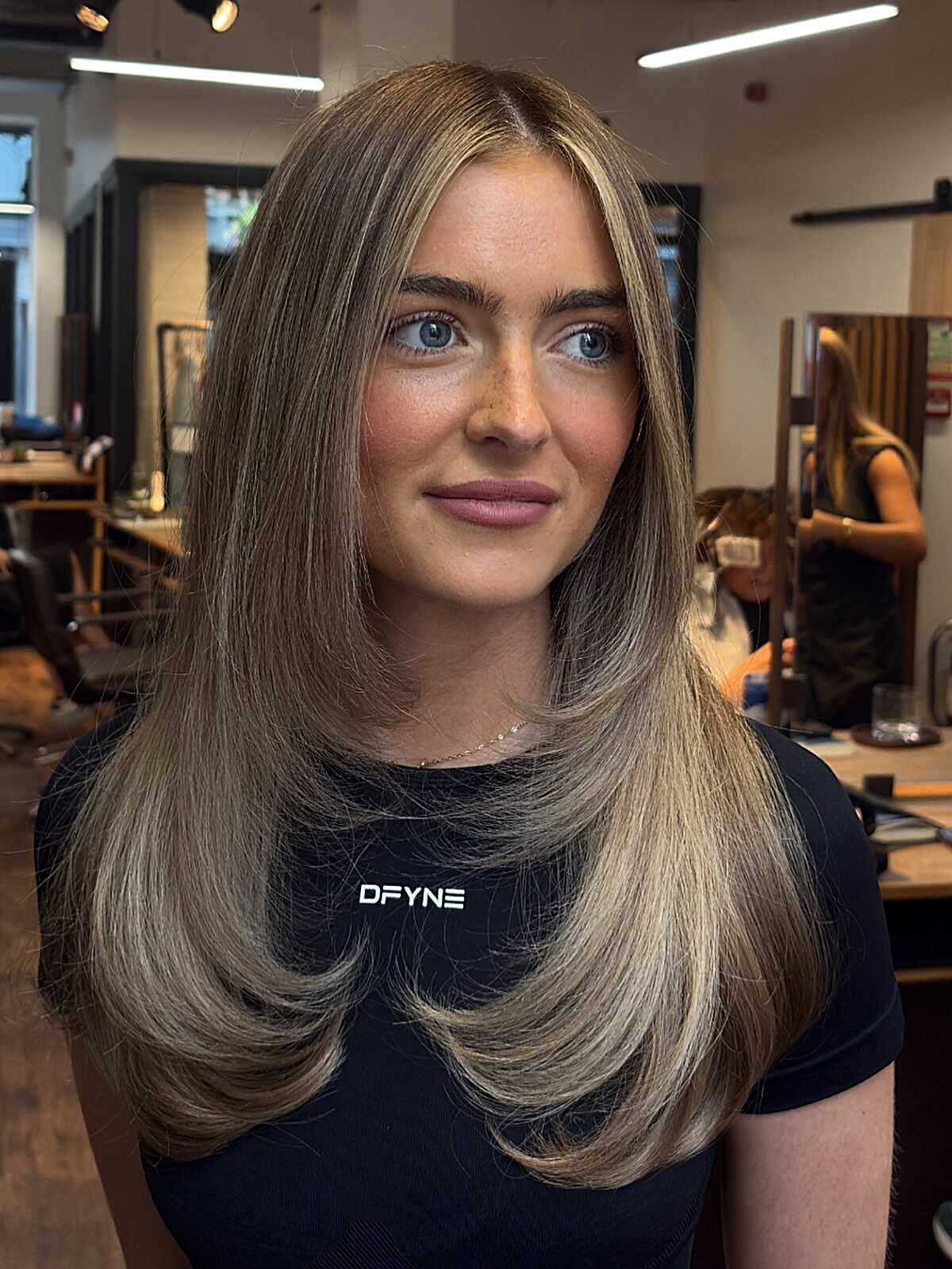 Long sleek layered hair with smoky brown and blonde tones.