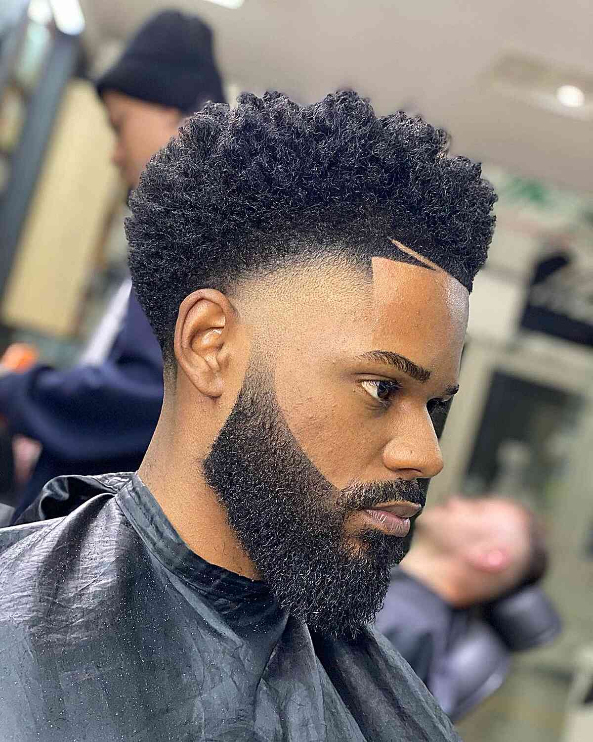 Tall curly top with a high fade and a full shaped beard.