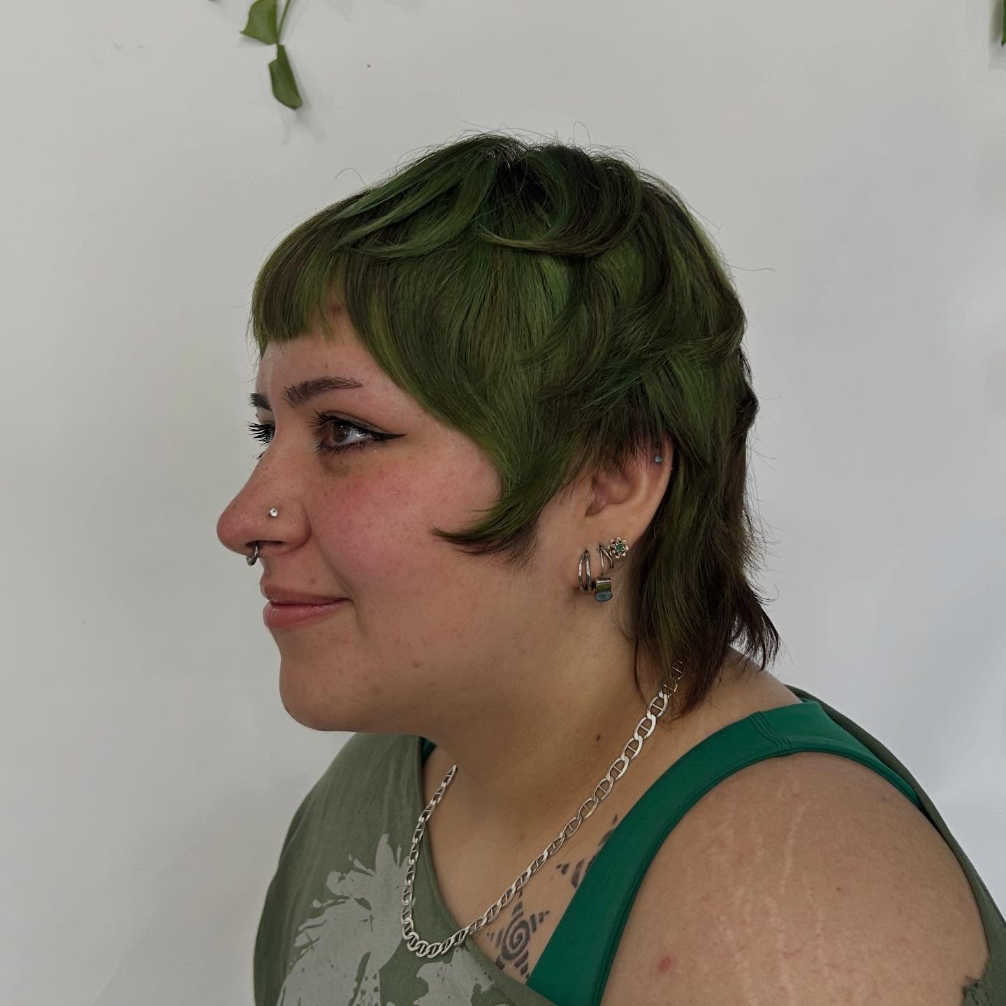Short green pixie with micro fringe, rounded crown, and tapered sides.