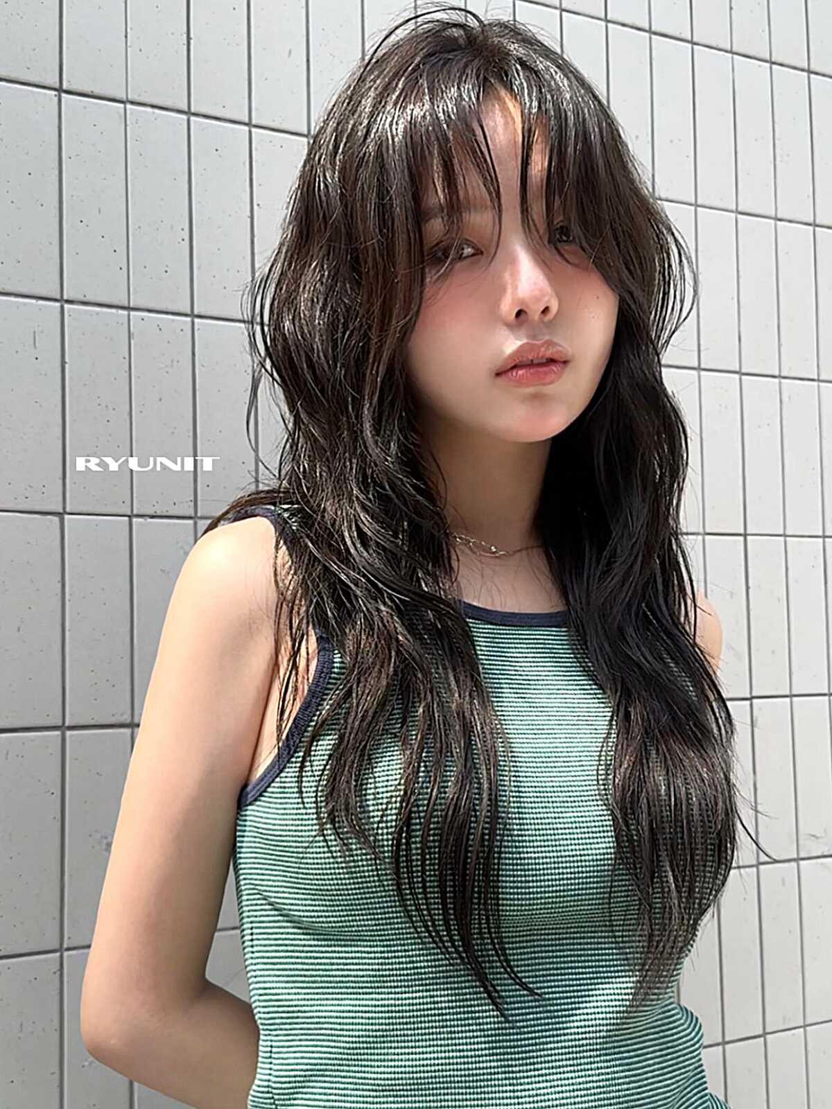 Long dark wavy hair with wispy curtain bangs and soft layers.