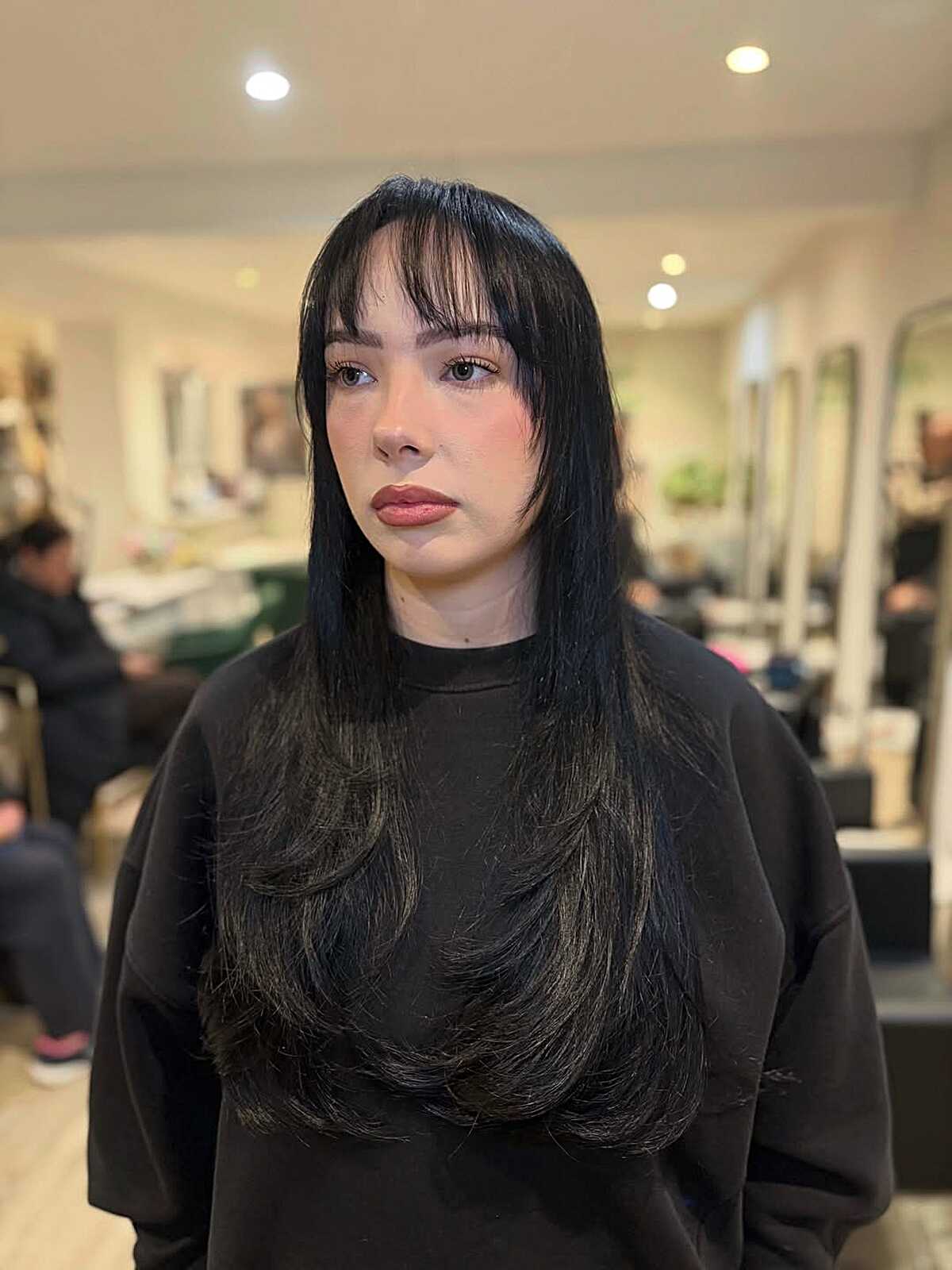 Long black hair with wispy straight bangs and subtle layers.