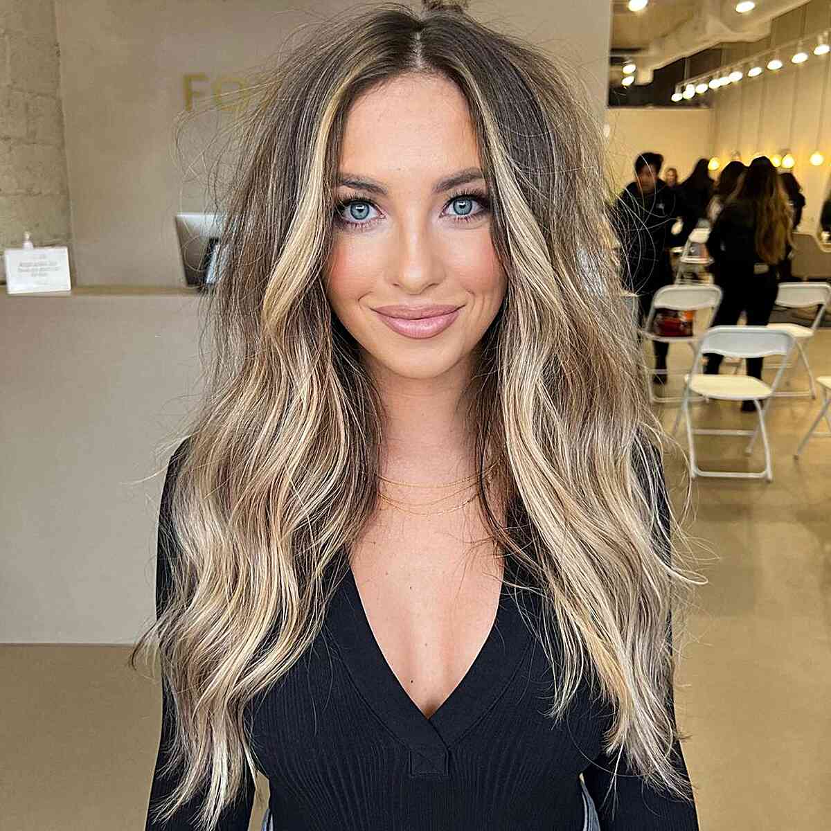 Long tousled brown hair with bright money-piece bronde highlights.