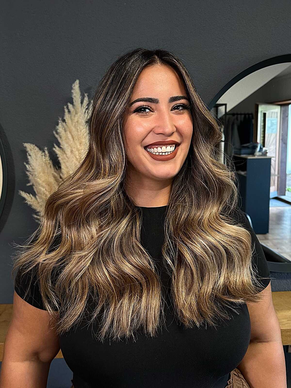 Long brunette waves with blonde face-framing highlights and dark roots.