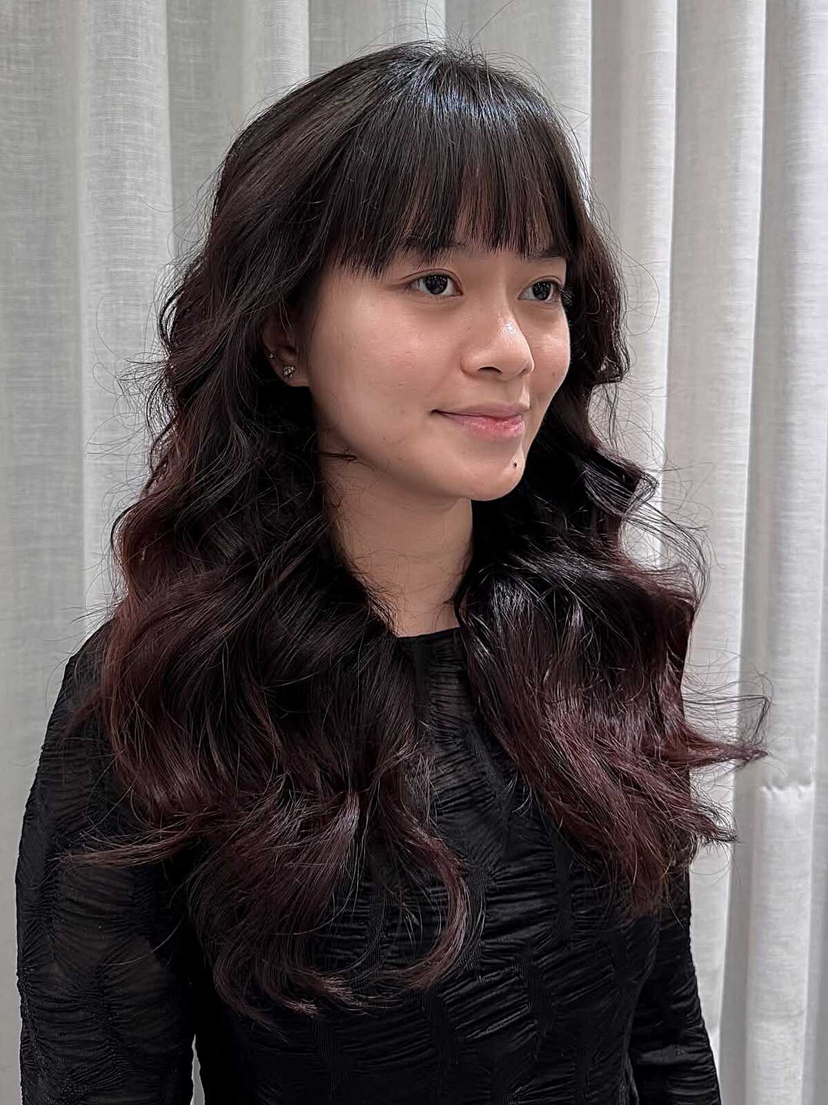 Long dark wavy hair with full bangs and burgundy ends.