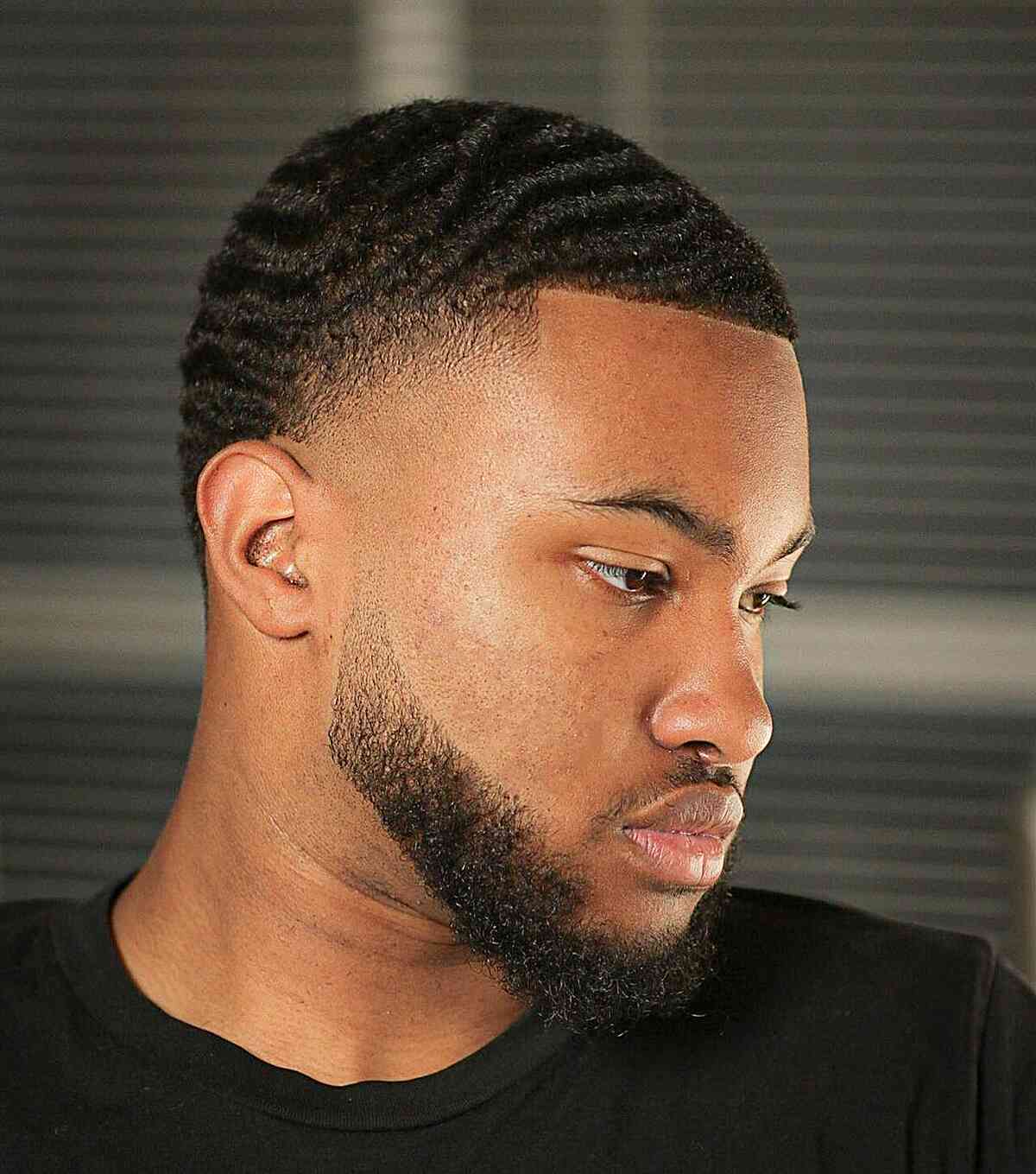 Short wavy pattern on top with a low fade and full beard.