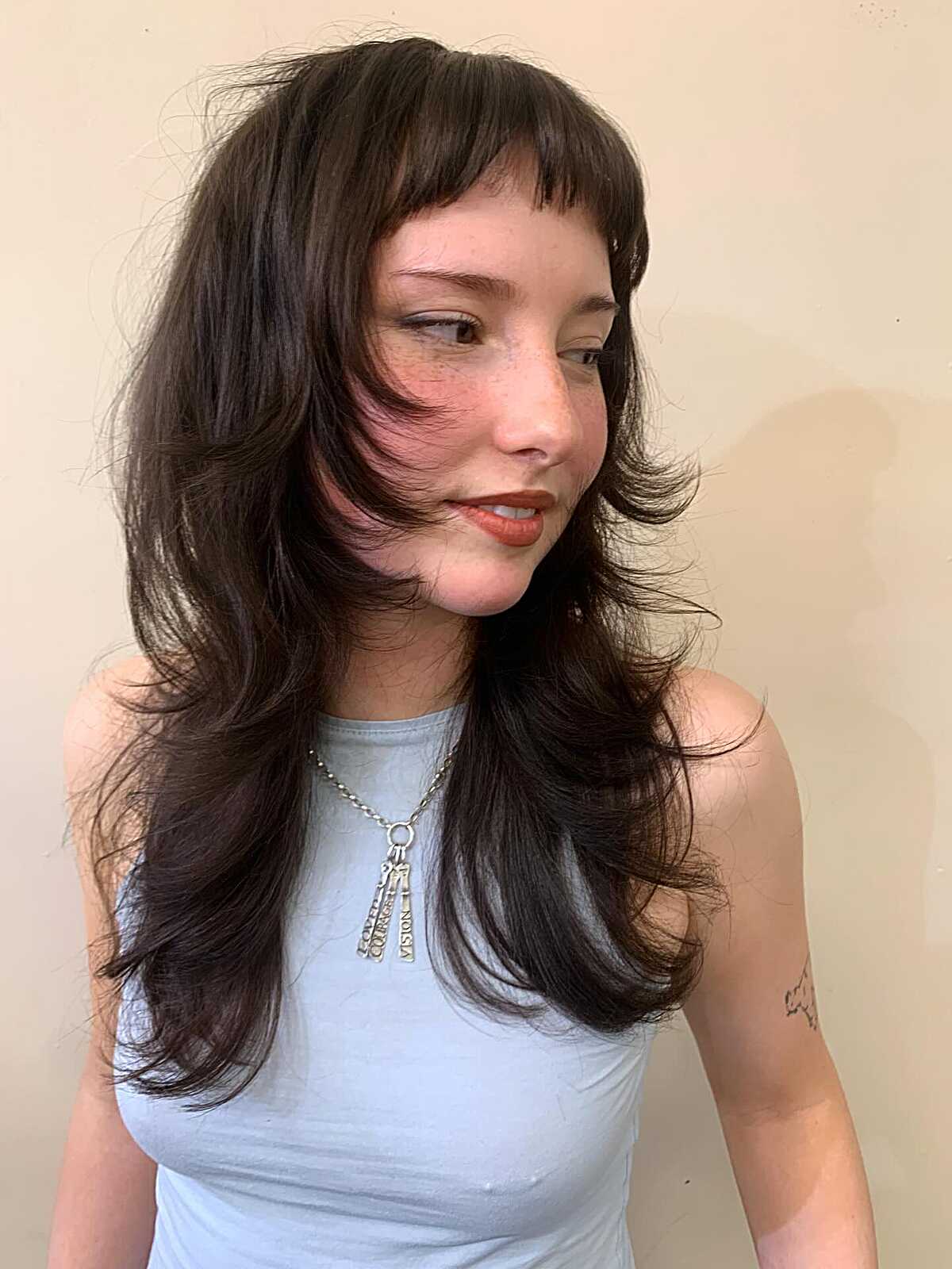 Long dark brunette hair with baby bangs and shaggy layers.