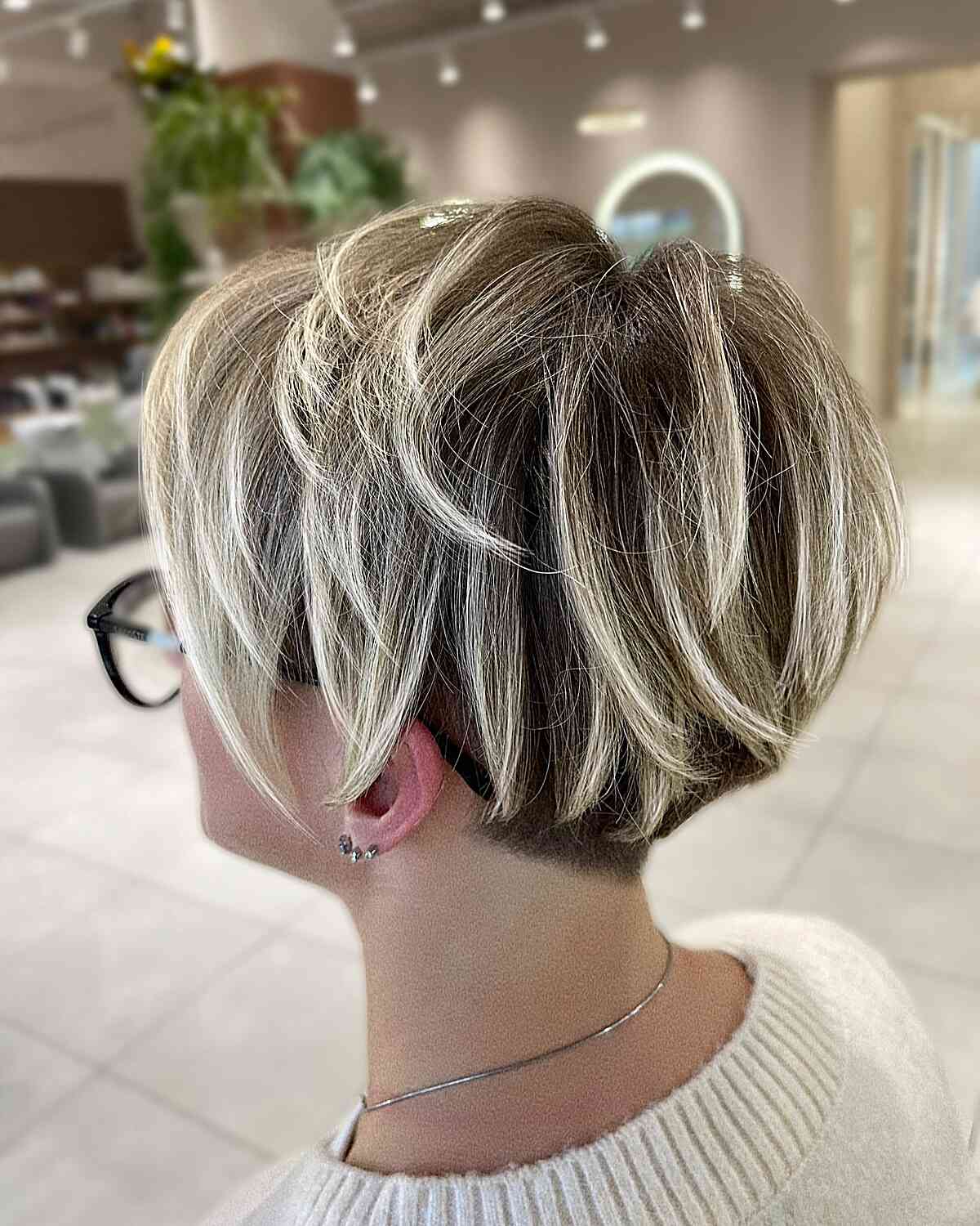 Short blonde pixie bob with highlights, roots, and soft texture.