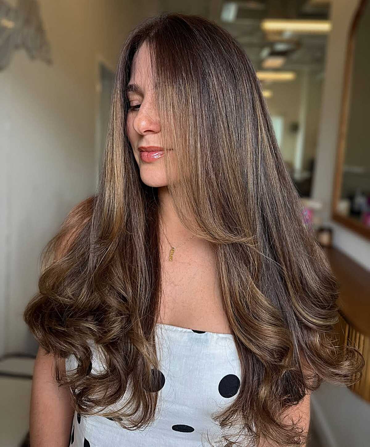 Long dark brown blowout curls with warm peekaboo lowlights.