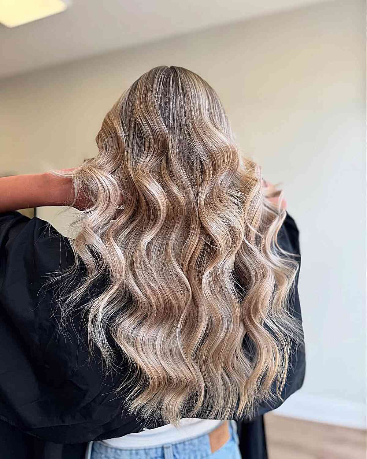 Very long blonde wavy hair with a darker root and loose bends.