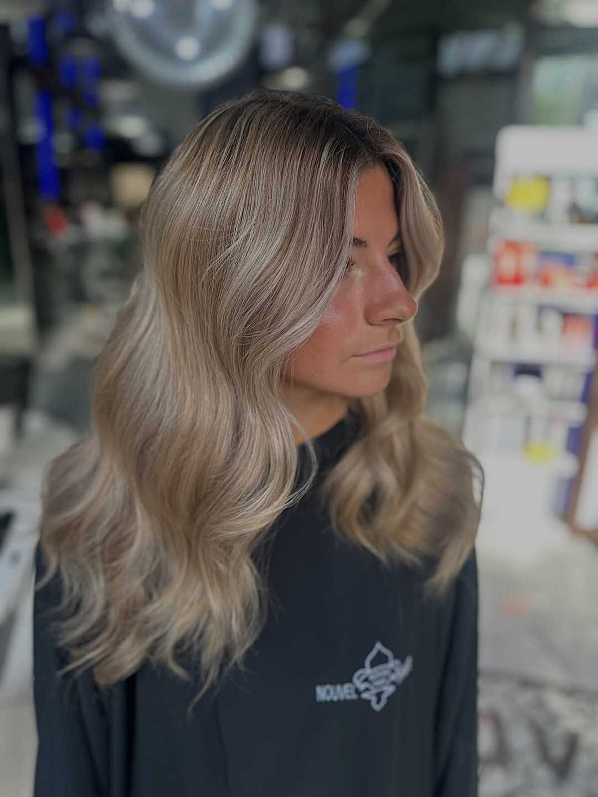 Medium wavy ash blonde hair with dark roots and loose movement.