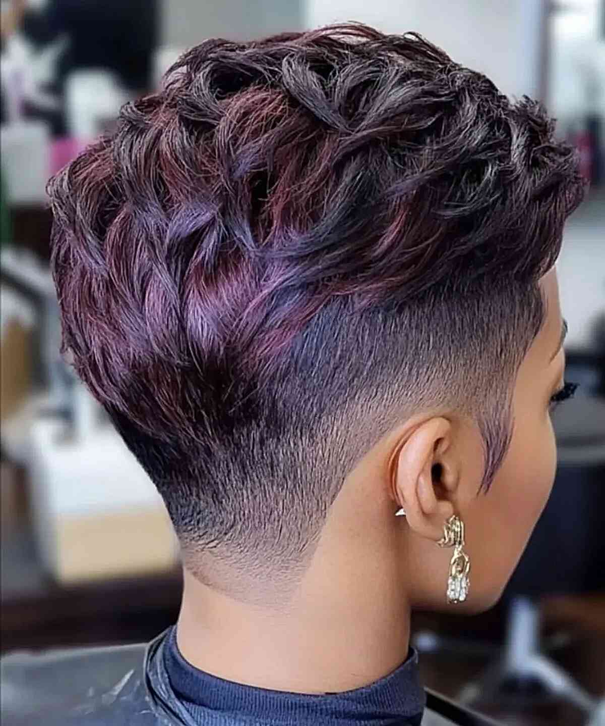 Short pixie with shaved sides, tousled top, and plum highlights.